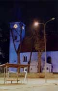 modře nasvícený kostel, v popředí pětka na skleněné zastávce